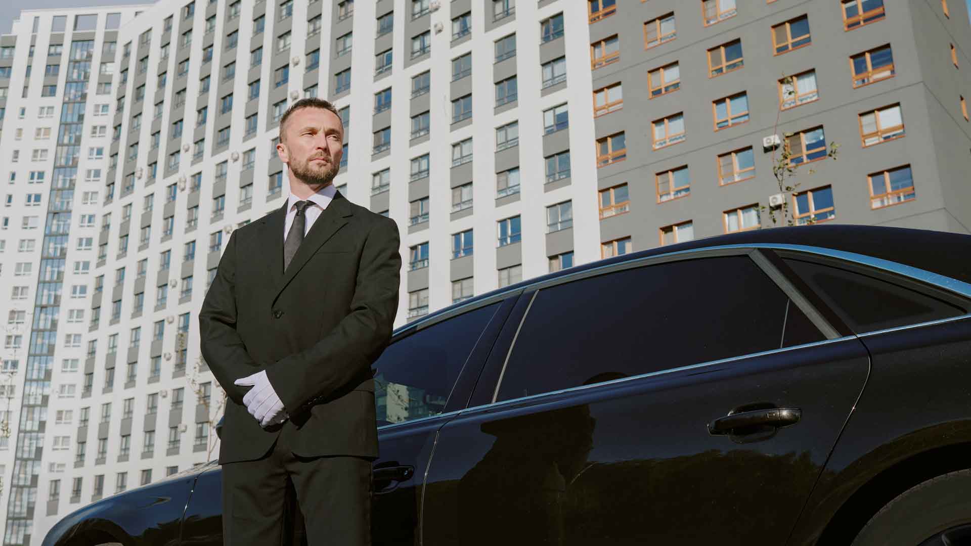 White-gloved chauffeur standing beside a luxury black vehicle